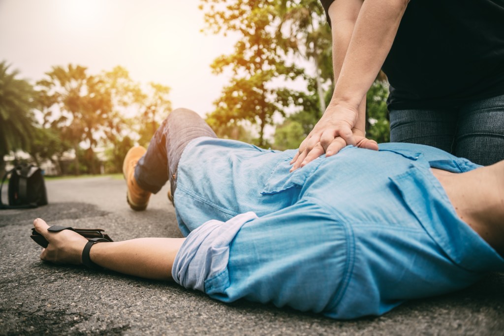 Person performing emergency first aid CPR on a man experiencing a heart attack or stroke